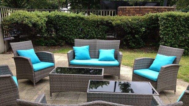 Outdoor wicker furniture with cushions, a glass table, and a brick wall in the background. - ibis Styles Paris Saint Denis Plaine (Saint-Denis)