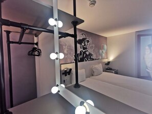 Una camera d'albergo con uno specchio trucco, luci, un letto e un affresco sulla parete.