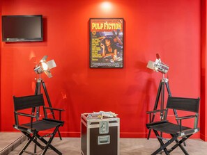 A room with red walls, two director's chairs, a table with magazines, and two mounted spotlights.