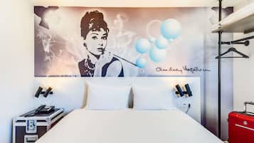 Una camera d'hotel con un letto, un grande murale e due valigie, una rossa e una nera.