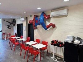 A dining area with red chairs and white tables, a mounted Spiderman sculpture, and a wall-mounted air conditioner.