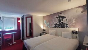 A hotel room with a bed, a desk, a chair, and a large wall mural. - ibis Styles Paris Saint Denis Plaine (Saint-Denis)