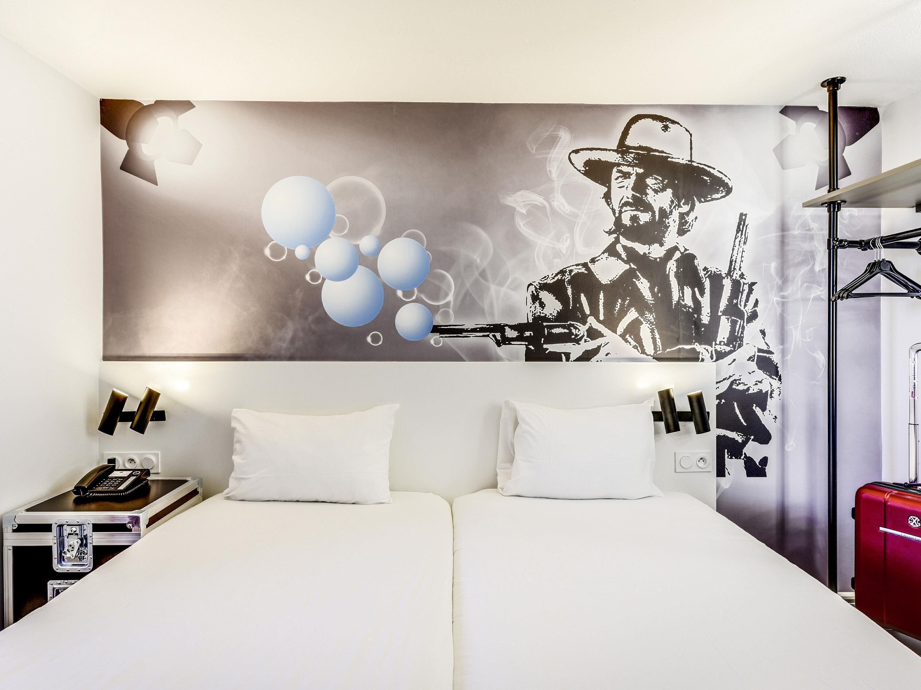 Une chambre d’hôtel comprenant un lit, deux oreillers, une table de chevet avec un téléphone et une lampe, et un mur orné d’un motif graphique.