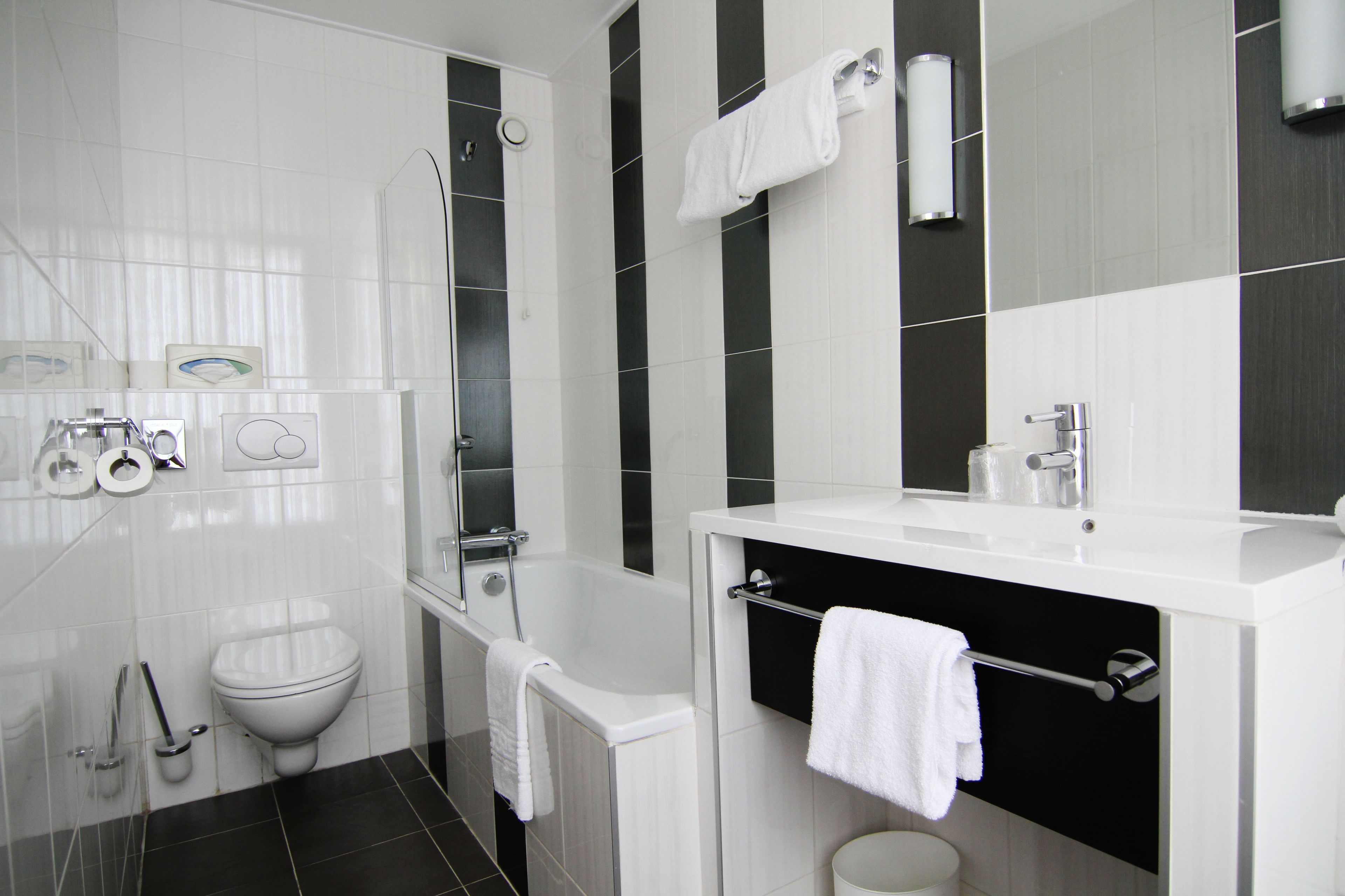 A modern bathroom with a white bathtub, a toilet, and a sink with a towel rack.