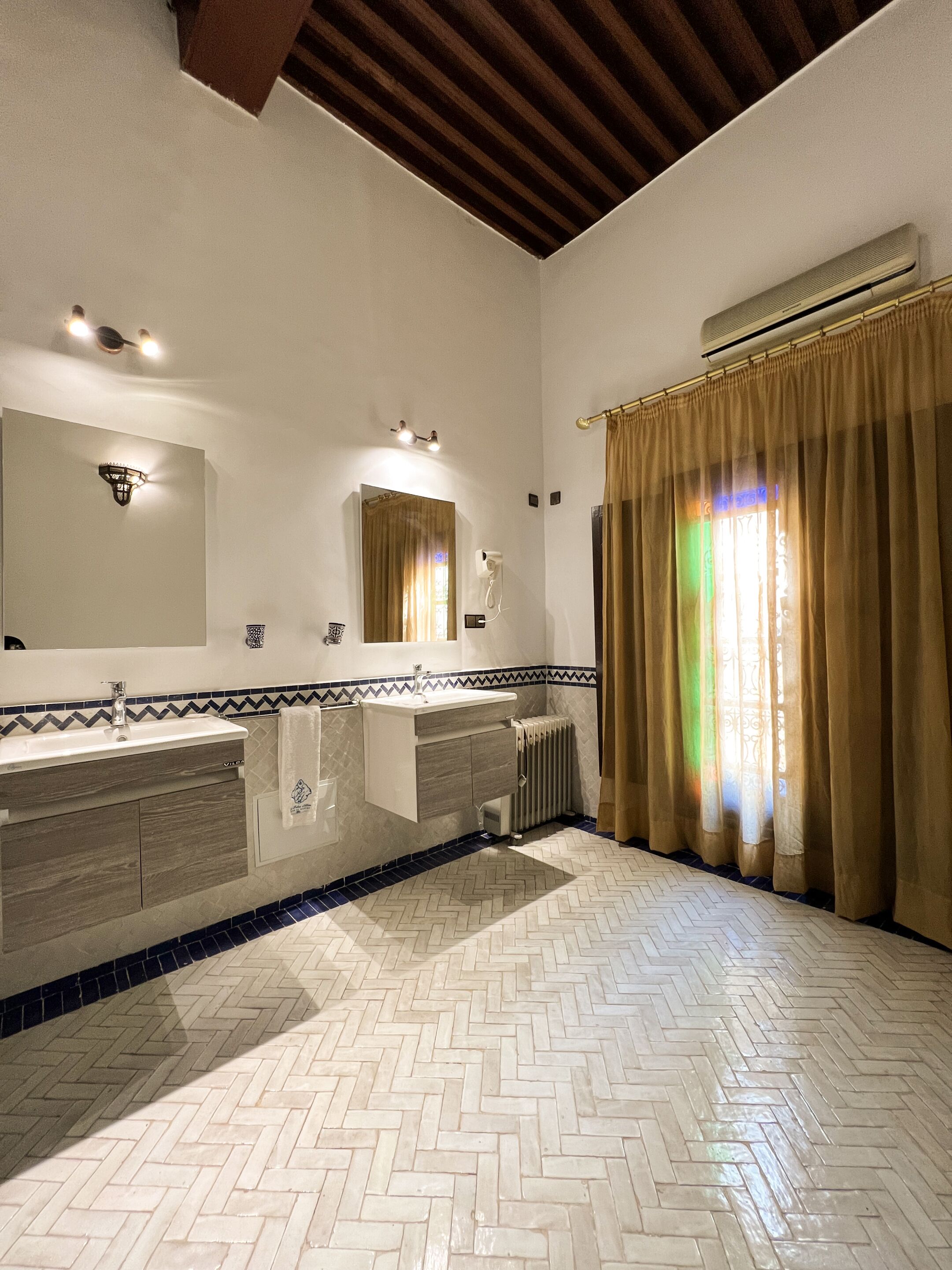 A bathroom with a herringbone floor, a large mirror, a vanity with a towel, and a radiator.