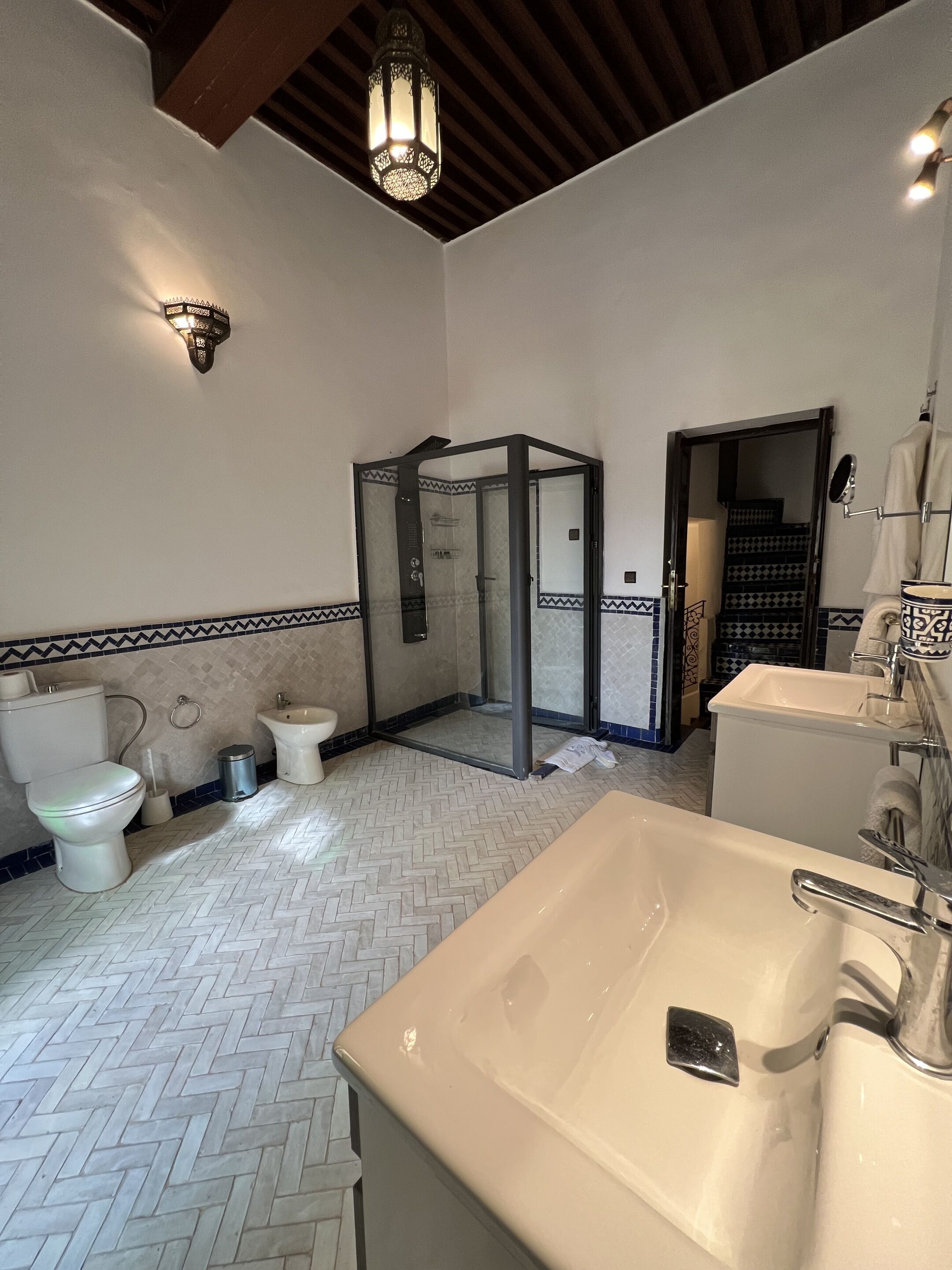 A bathroom with a herringbone floor pattern, a white sink, a toilet, and a shower enclosure.