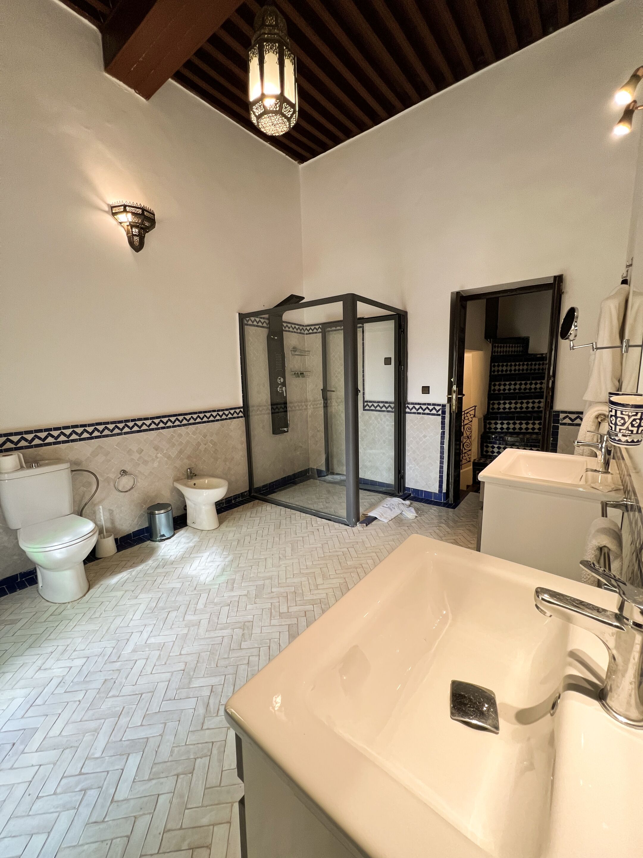 Un baño con piso de diseño espiga, un lavamanos grande blanco, un inodoro y un box de ducha.
