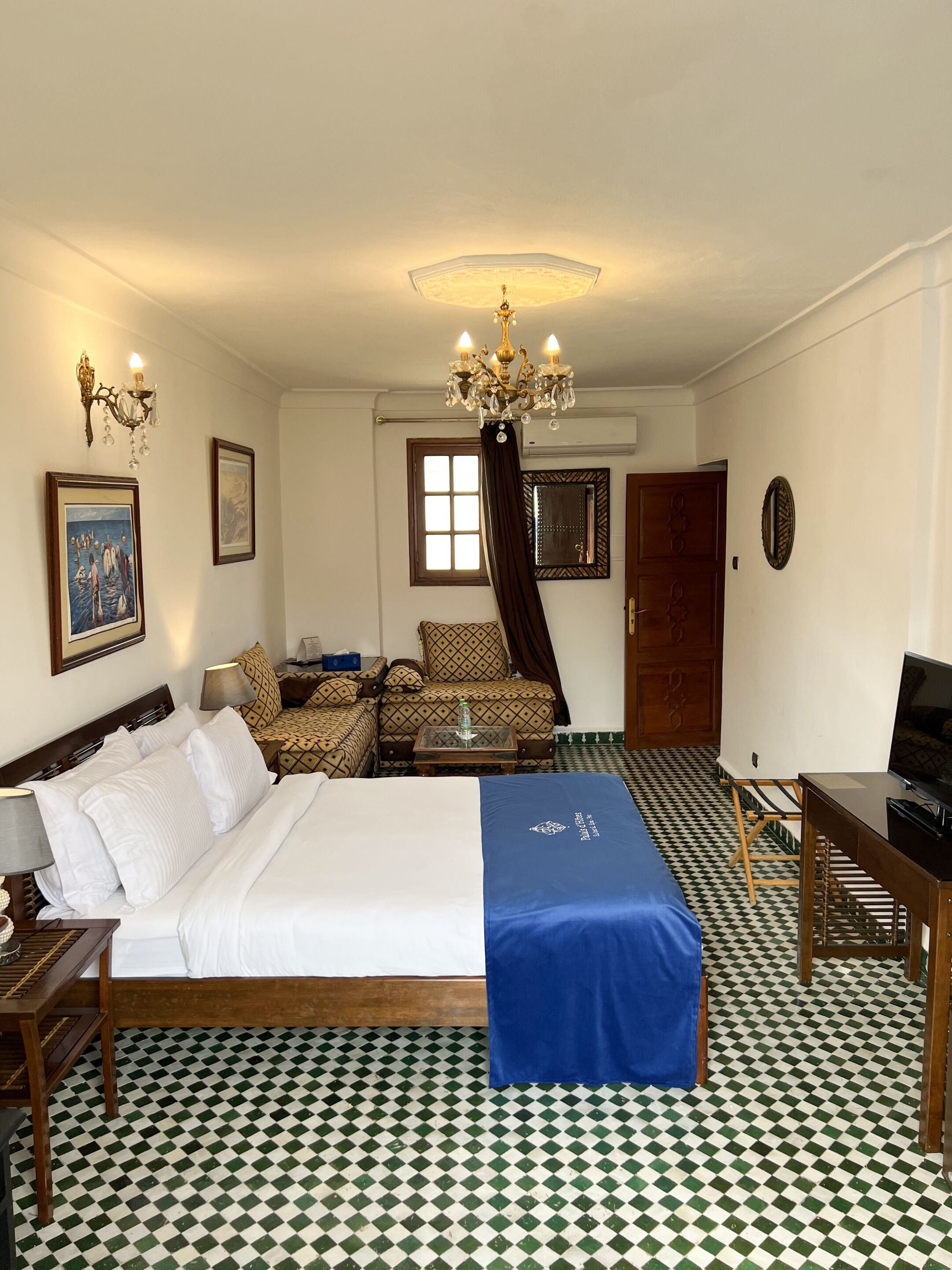 Una habitación de hotel con cama, sofá, televisión, escritorio y candelabro.