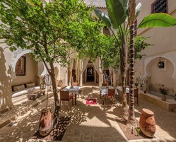 An outdoor courtyard with tables and chairs, surrounded by arches and plants.