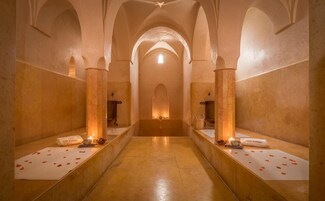 A corridor with arched ceilings and a central light source. There are benches with towels and candles on either side.