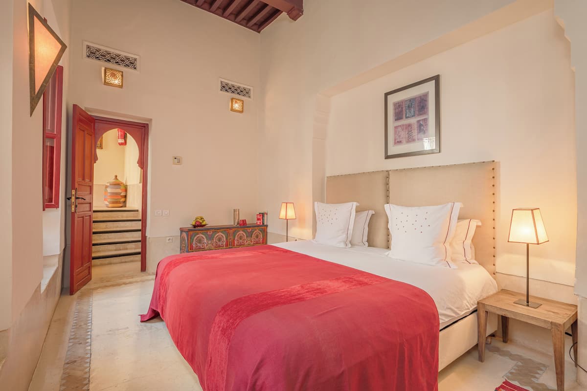 A bedroom with a large bed, a nightstand, a lamp, a framed picture on the wall, and a decorative cabinet.