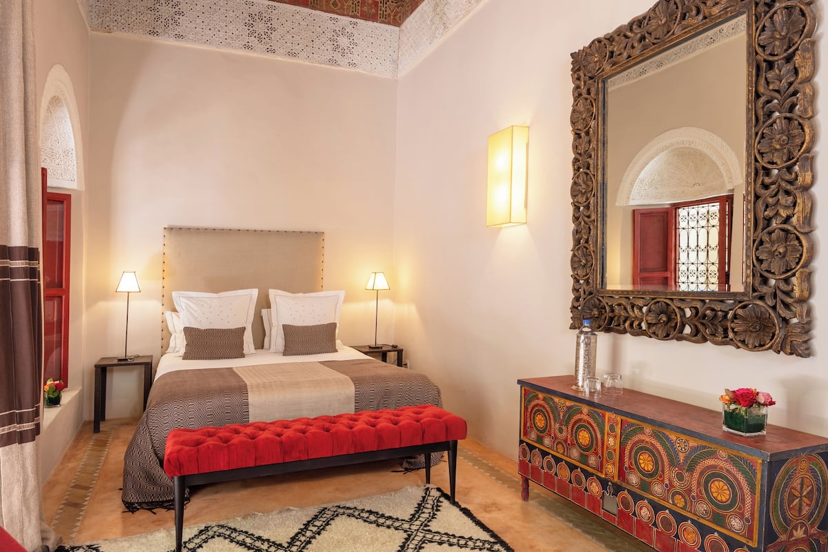 A bedroom with a large bed, bedside lamps, a bench, a decorative dresser, and a mirror.