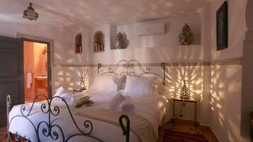 A bedroom with a bed, bedside tables, a nightstand, a decorative vase, and a wall-mounted air conditioner.