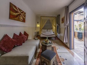 A hotel room with a bed, a sofa, a small table with fruit, and a view of the outside. - Palais Tinmel Marrakech (Marrakech)