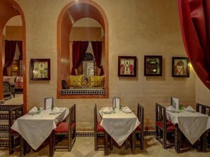 A restaurant with tables set for dining, framed artwork on the walls, and a decorative window. - Palais Tinmel Marrakech (Marrakech)