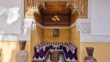 Una habitación con techo estampado, un sofá con cojines, una mesa con un jarrón y un jarrón grande en el suelo.