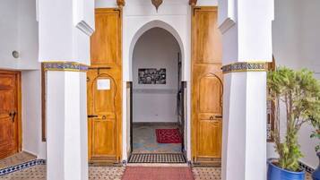 A hallway with a tiled floor, wooden doors, and a red carpet leading to a room with a patterned rug.