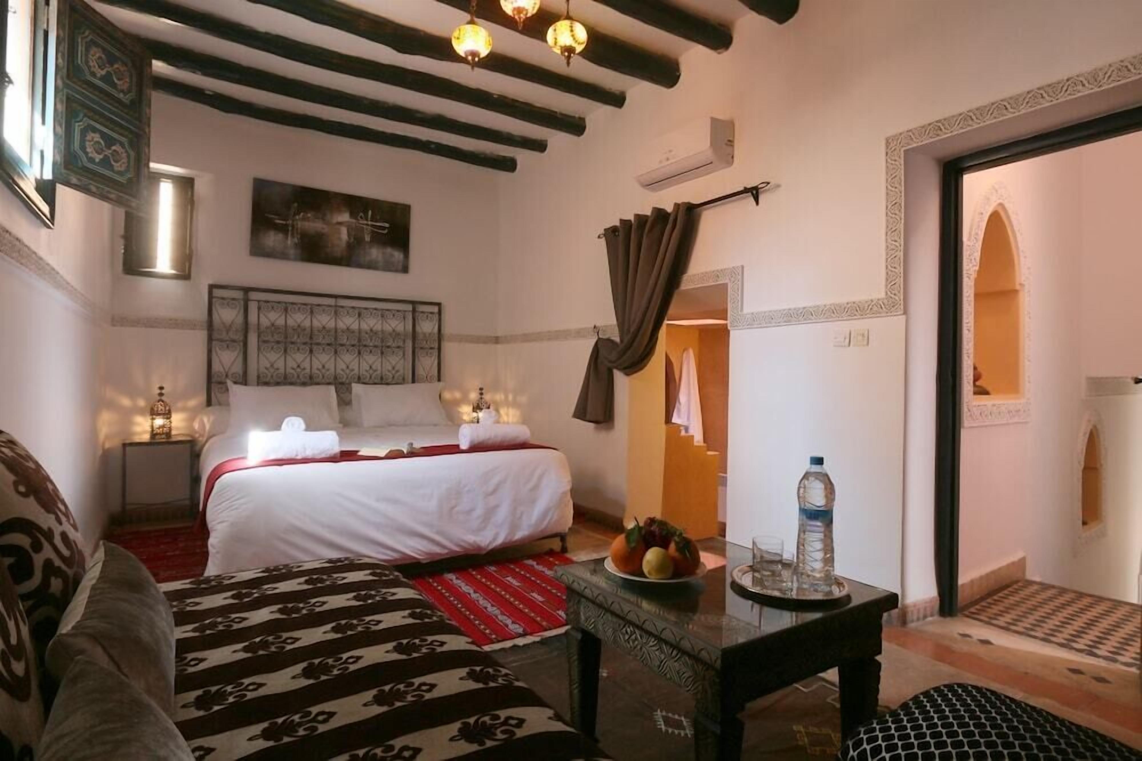 Un dormitorio con cama, mesitas de noche, aire acondicionado de pared, un adorno en la pared y una puerta que da a otra habitación.