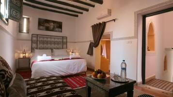 Un dormitorio con cama, mesitas de noche, aire acondicionado de pared, un adorno en la pared y una puerta que da a otra habitación.