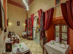 A dining area with tables set for guests, a staircase, and a view through a window with curtains. - Palais Tinmel Marrakech (Marrakech)