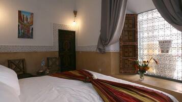 A hotel room with a bed, a painting on the wall, a door, and a window with curtains.