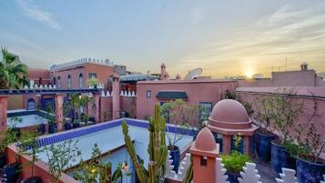 A courtyard with potted plants, a cactus, and a building with a dome and satellite dishes.