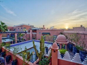 A courtyard with potted plants, a cactus, and a building with a dome and satellite dishes. - Palais Tinmel Marrakech (Marrakech)