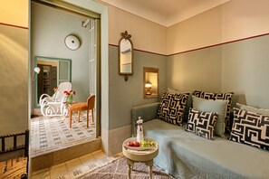 A cozy room with a sofa, a small table with a fruit bowl, a mirror, and a chair.