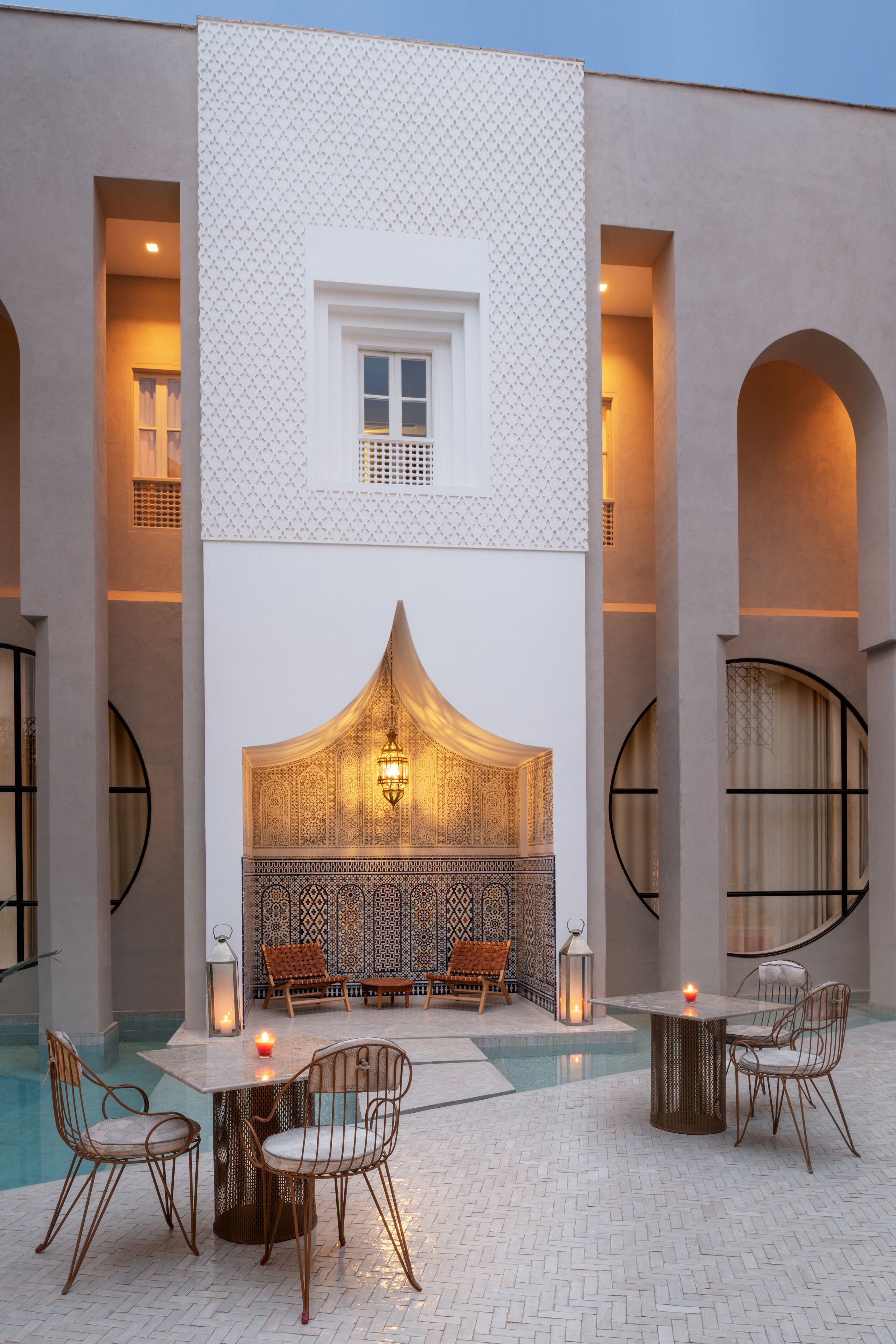 Une cour avec une piscine, un espace détente et un mur décoratif orné de motifs complexes.