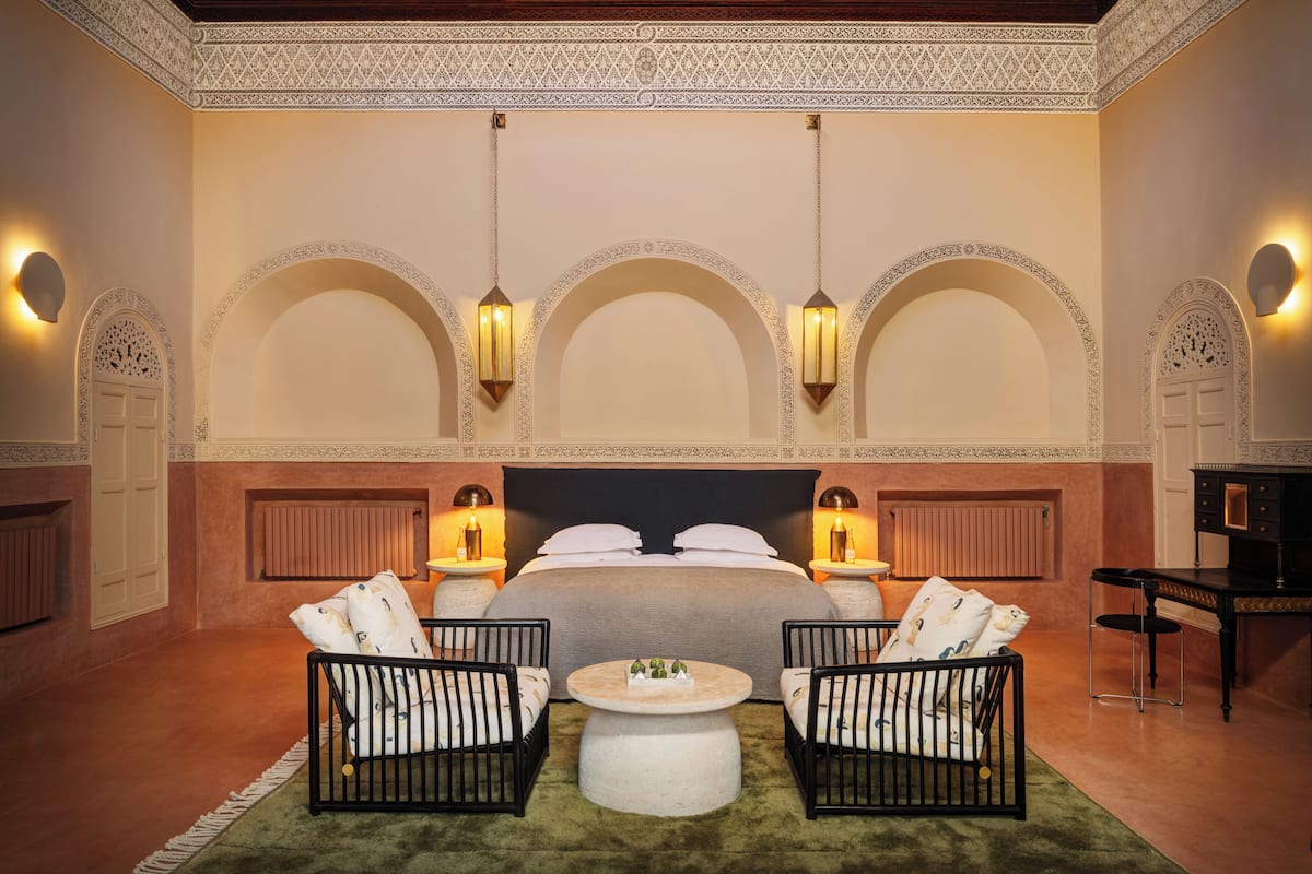 A bedroom with a large bed, two bedside tables, two wall-mounted lamps, and two chairs with a round coffee table.