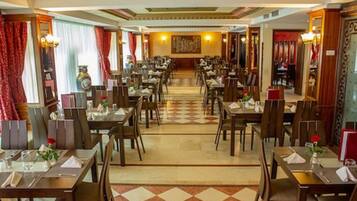 A hotel dining area with multiple tables and chairs, a checkered floor, and a central wall with a clock and artwork.