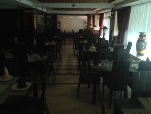 A restaurant with a checkered floor, tables with napkins, and a vase on the counter. - Helnan Chellah Hotel (Rabat)