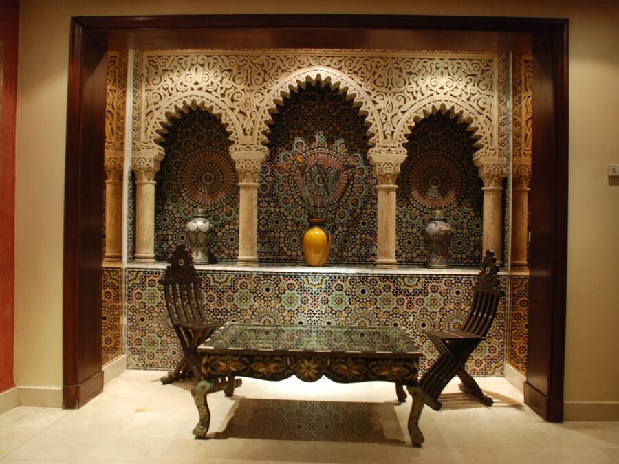 Un interior tradicional con un papel tapiz estampado, una mesa central y dos sillas.