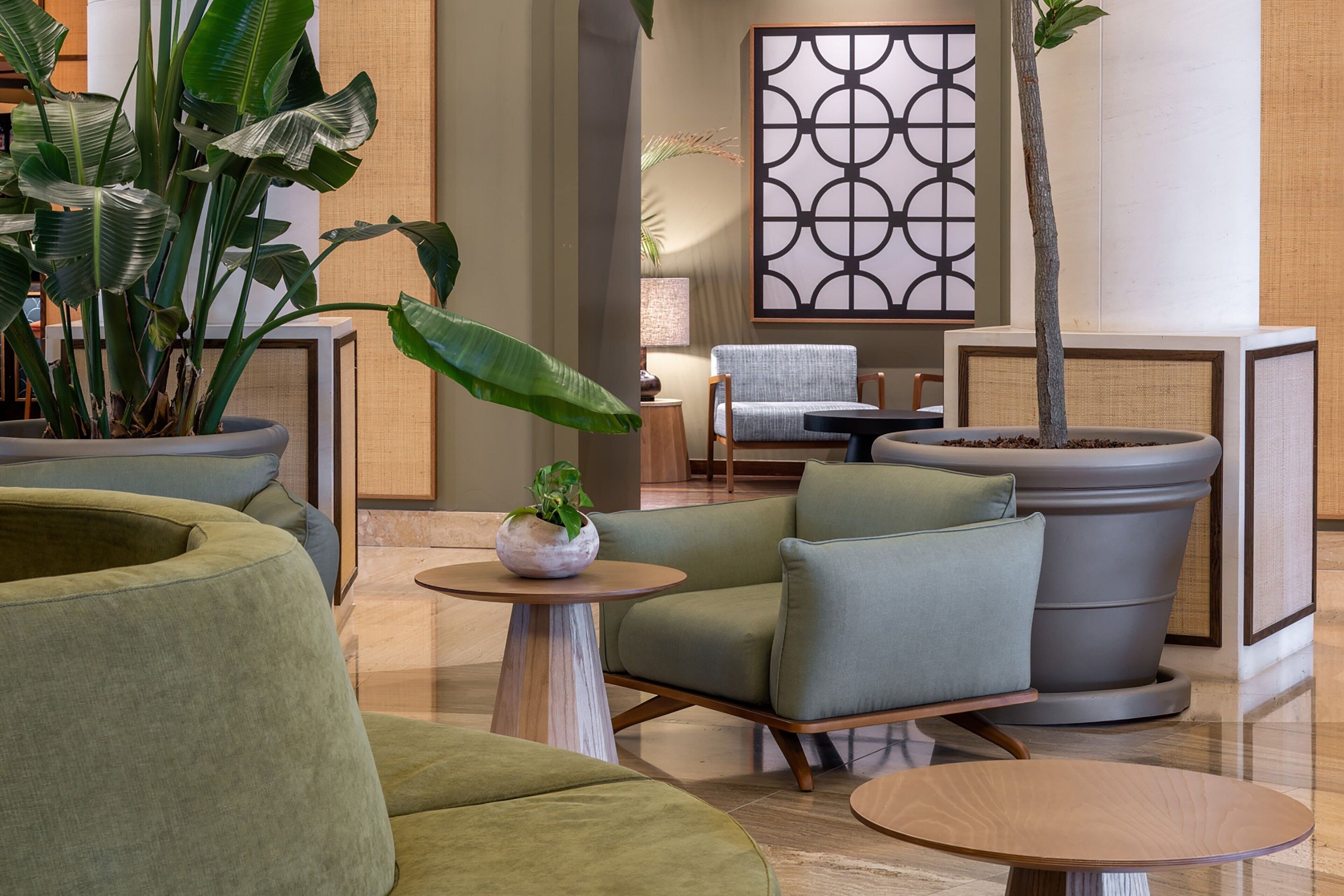 Un espace de détente moderne avec des canapés verts, une table ronde en bois et des plantes en pot.