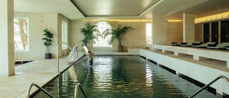 Una amplia piscina interior con agua cristalina, rodeada de paredes de piedra y plantas en macetas.