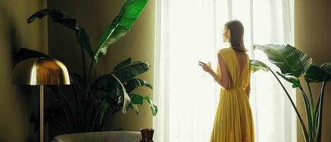 A room with a large window, a sofa, a table, and a potted plant.
