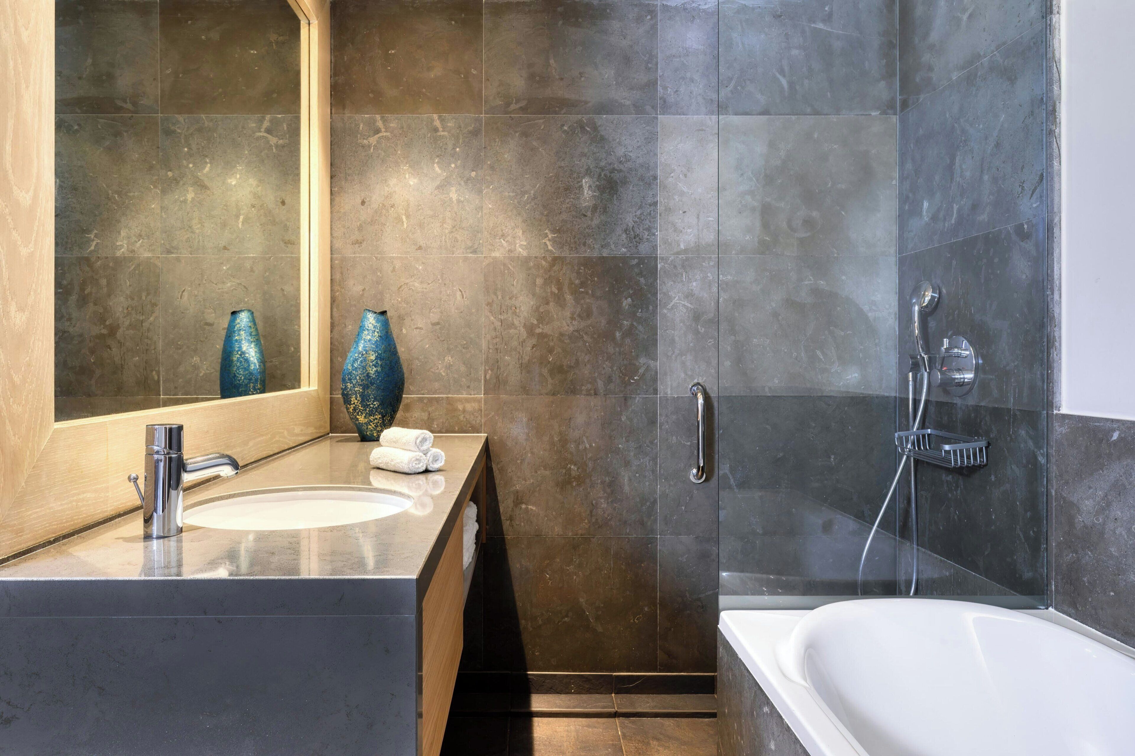 A modern bathroom with a marble sink, a large mirror, and a walk-in shower.