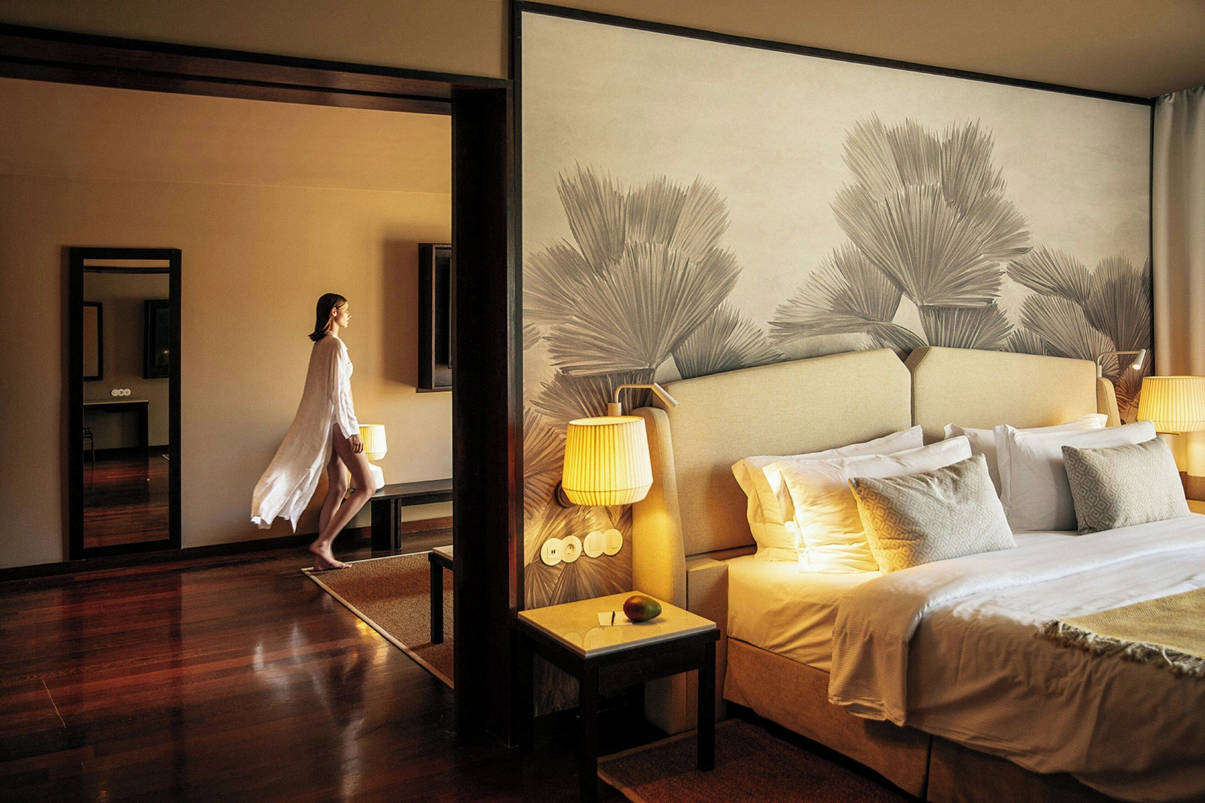 Une chambre d’hôtel avec un grand lit, une table de chevet, une lampe et un mur orné d’un grand tableau abstrait.