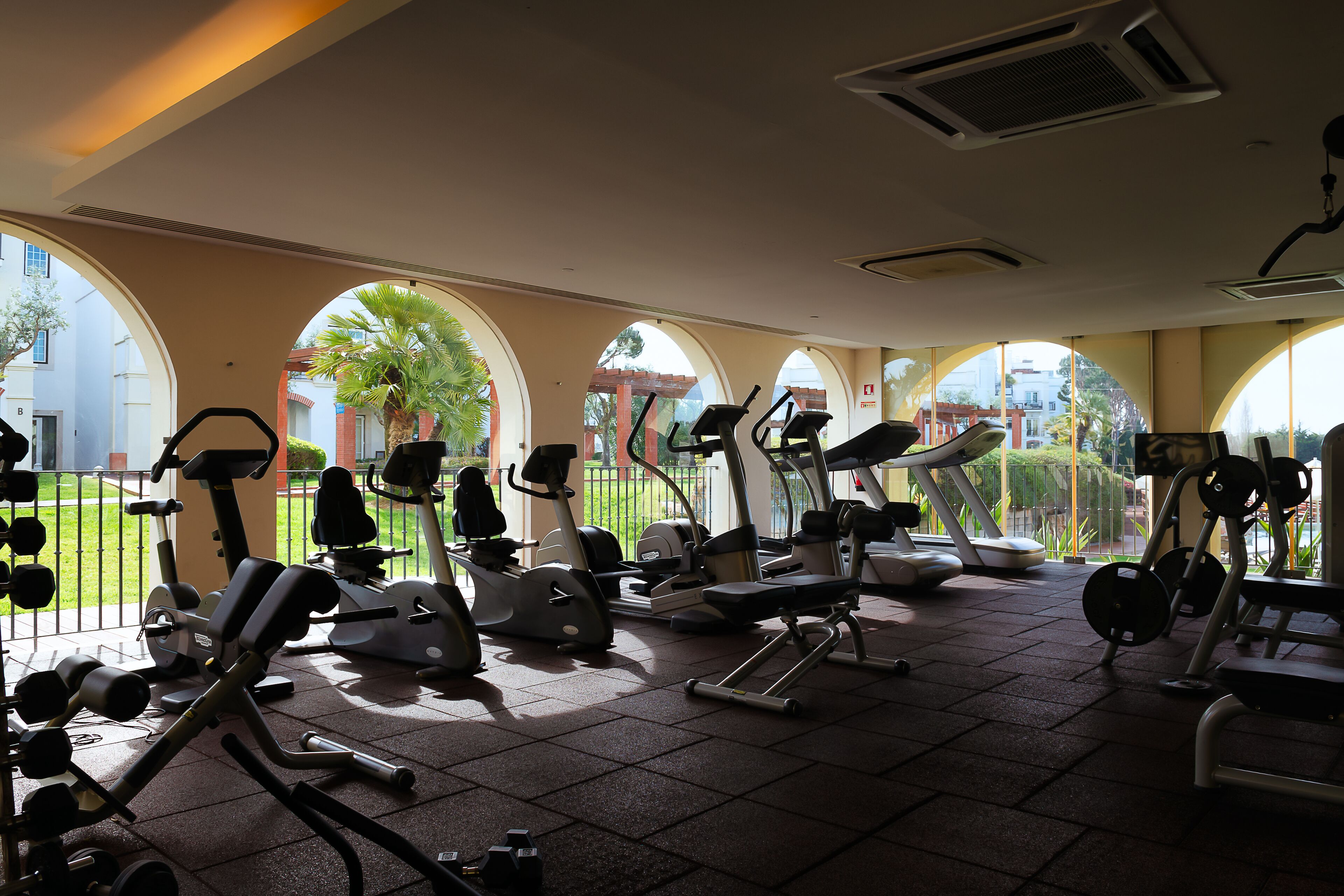 Un gimnasio con equipo de ejercicio diverso, ventanas amplias y vistas al exterior.
