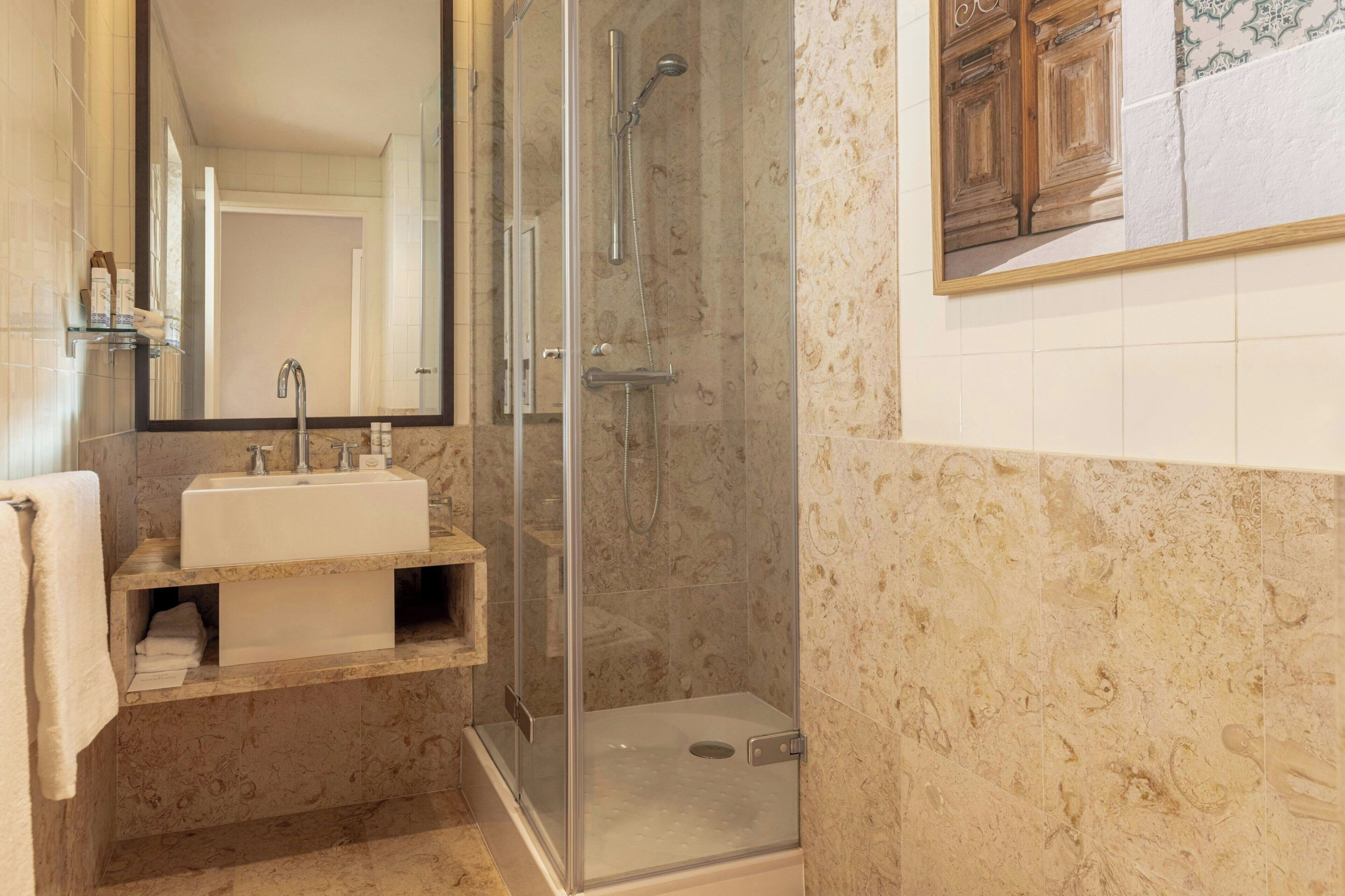 A bathroom with a glass-enclosed shower, a sink with a mirror, and a tiled wall.