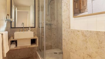 A bathroom with a glass-enclosed shower, a sink with a mirror, and a tiled wall.