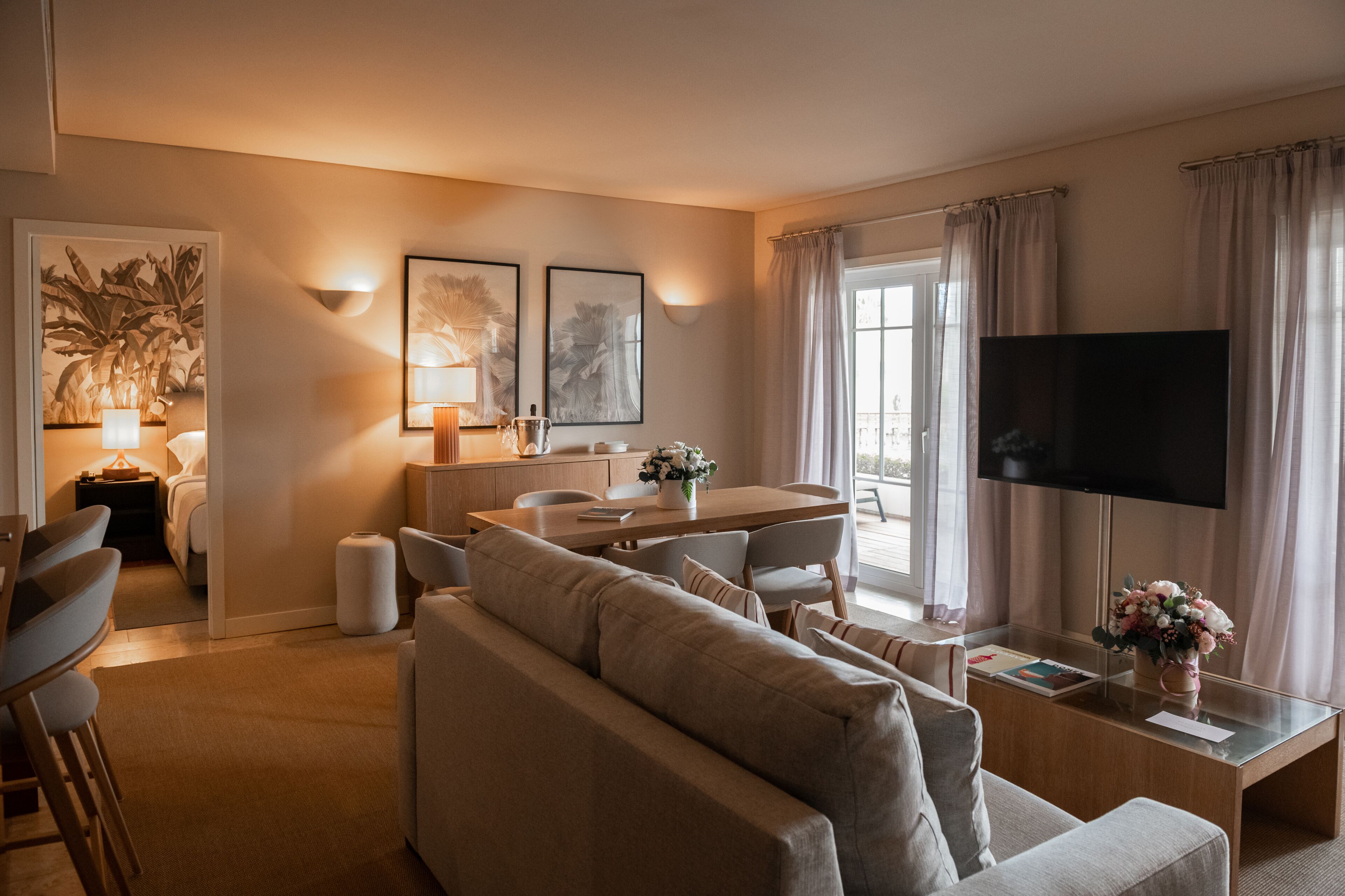 Un salon moderne avec un canapé, une table à manger et un téléviseur. Les murs sont ornés de tableaux encadrés et il y a une fenêtre avec des rideaux.