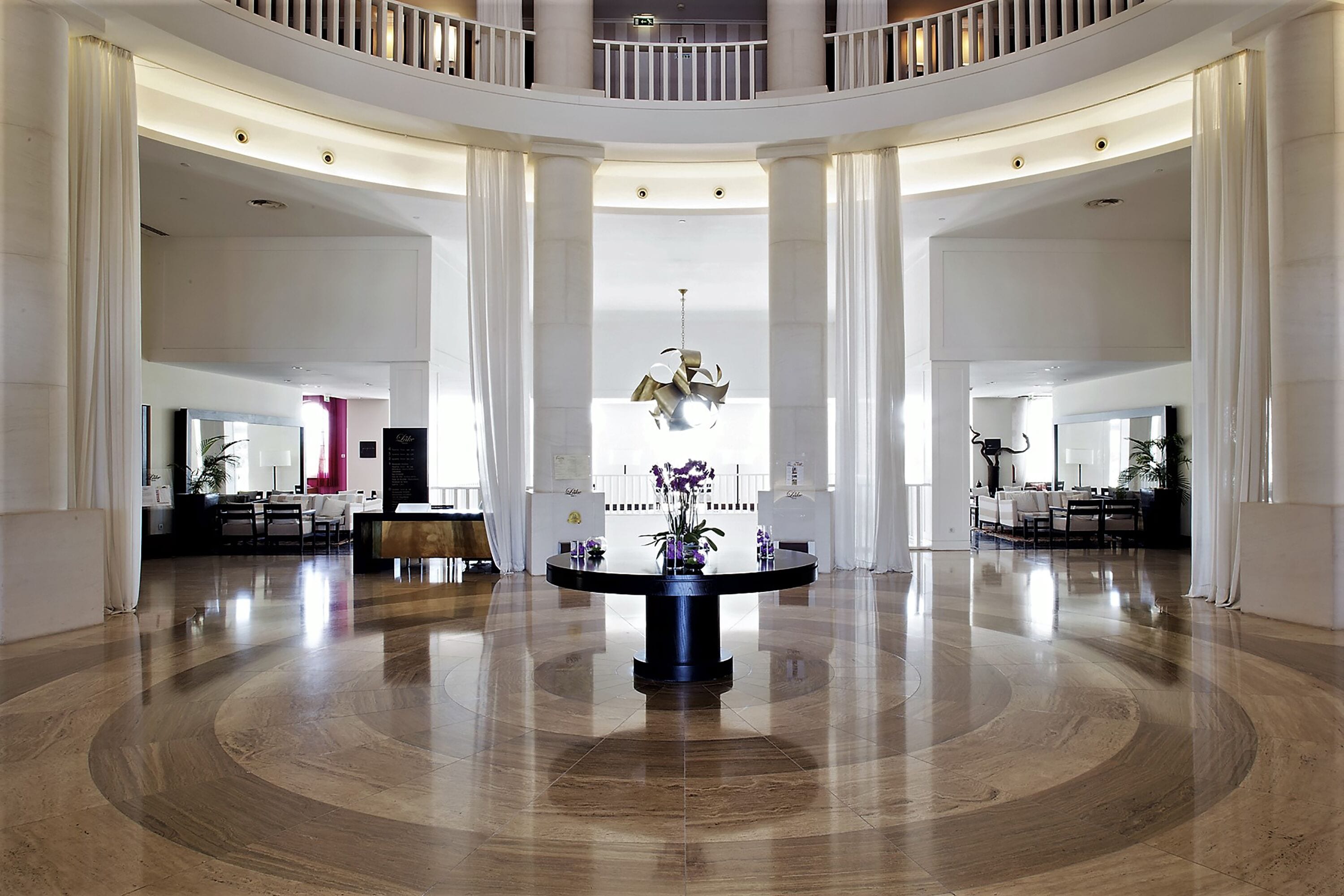 Un hall d’entrée spacieux avec une grande table ronde au centre, de hauts plafonds et un balcon.