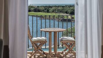 Un balcón con una mesa redonda de madera y dos sillas acolchadas, con vistas a un cuerpo de agua y un campo de golf.