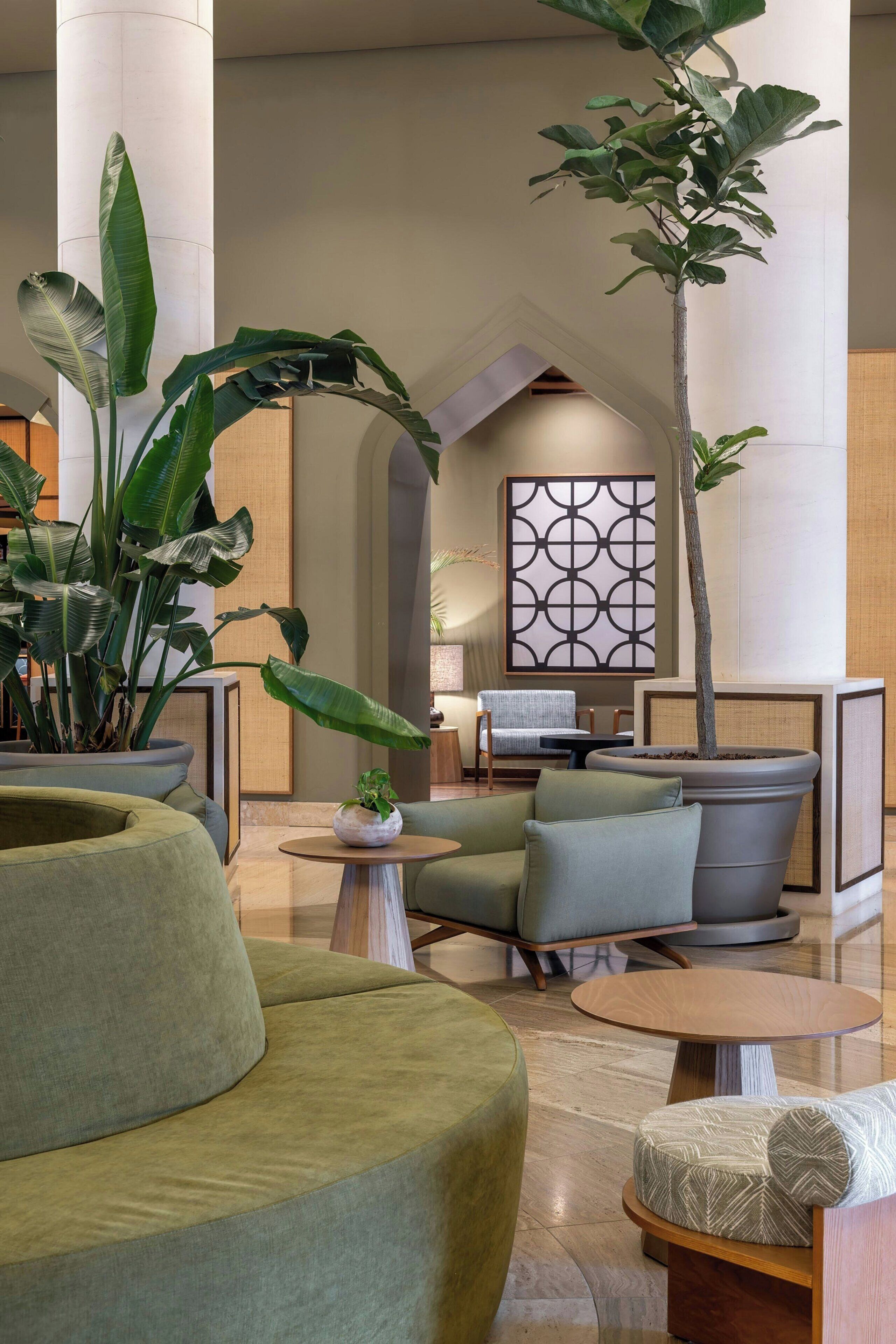 Un espacio lounge moderno con una planta en maceta grande, asientos cómodos y un panel decorativo en la pared.