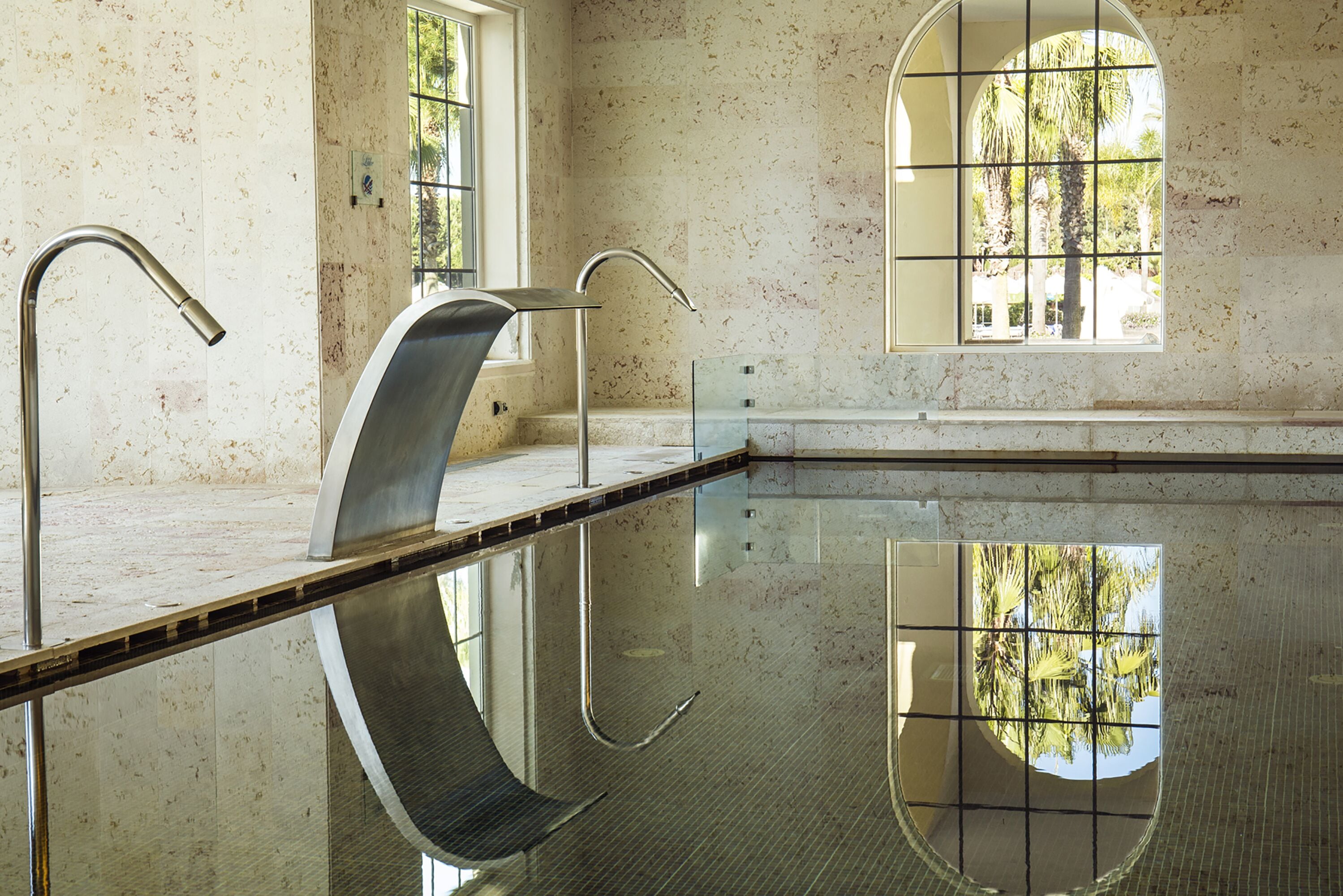 Una piscina interior moderna y limpia con paredes de vidrio transparente y suelo de baldosas.
