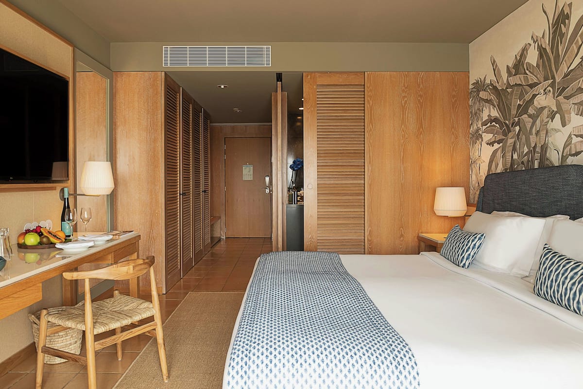 A hotel room with a bed, a desk with a chair, a television, and a large window.