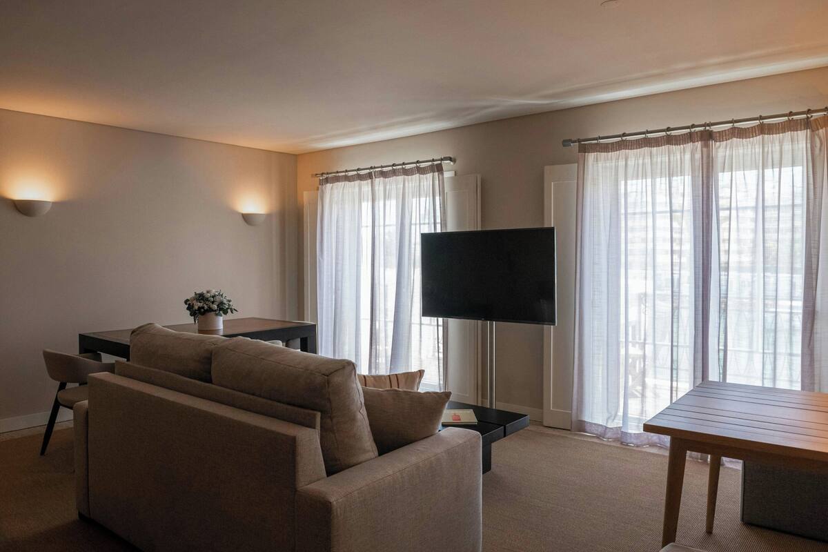 A living room with a sofa, a TV, a table, and curtains.