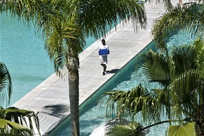 A man walking on a wooden deck over a pool, surrounded by palm trees.
