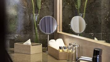A bathroom with a marble sink, two mirrors, a tissue box, and a vase with flowers.